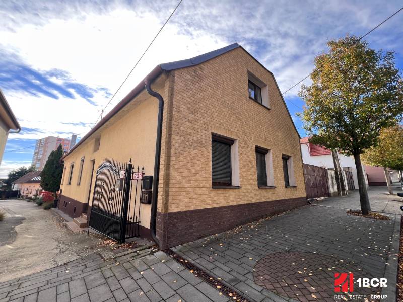 A house in Bratislava-Rača with a sloped roof, interlocking pavement, and trees along the walkway.