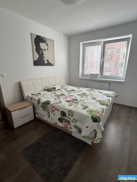 Bedroom in a two-room apartment with a wood-patterned floor and a picture on the wall.