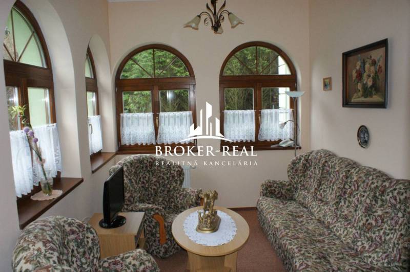Living room with a floral sofa set, arched windows, and decorative paintings.