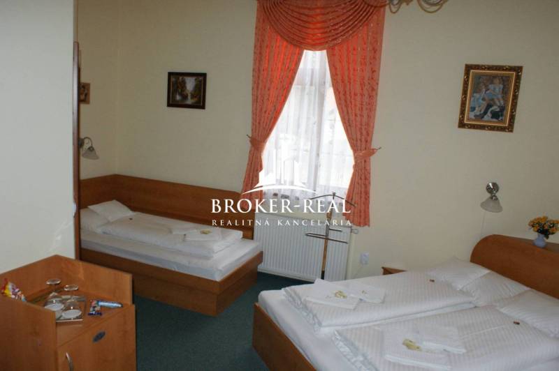 A hotel room with two beds, curtains, and paintings on the walls.