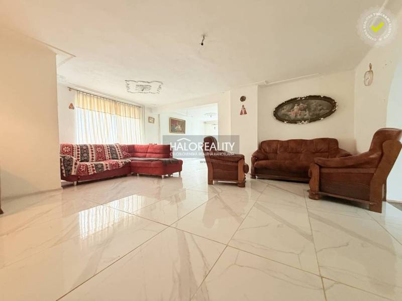 A bright living room in a family house with tiles, a red sofa, and brown armchairs.