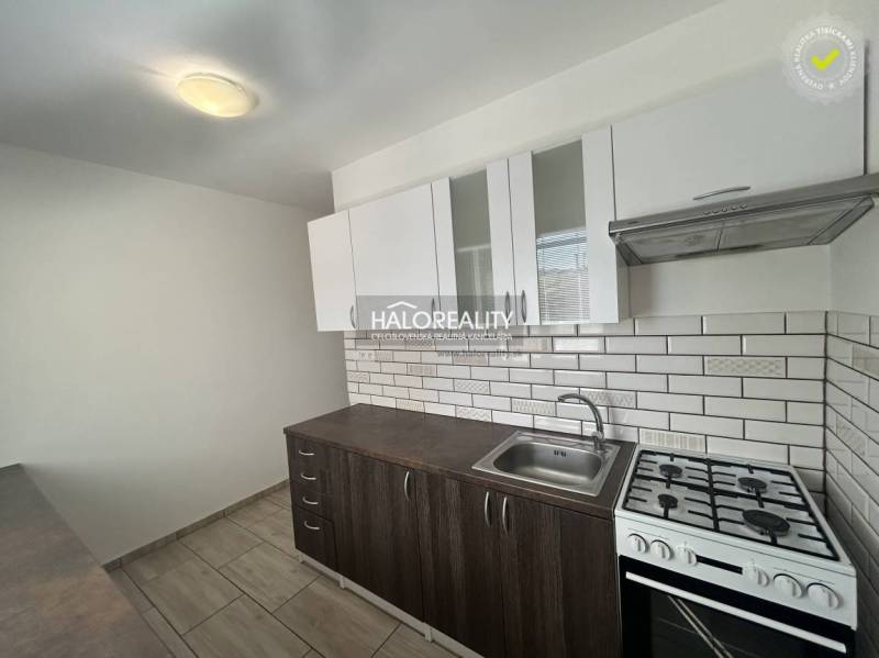 A kitchen in a 3-room apartment with white tiles and a wooden decor floor.