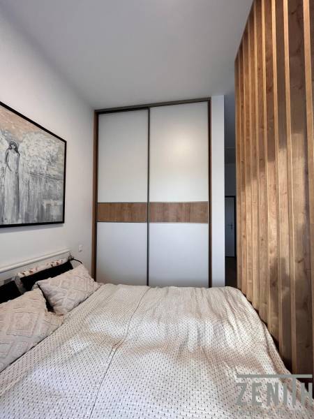 A bedroom with a bed, a painting, and a wardrobe in a studio apartment.