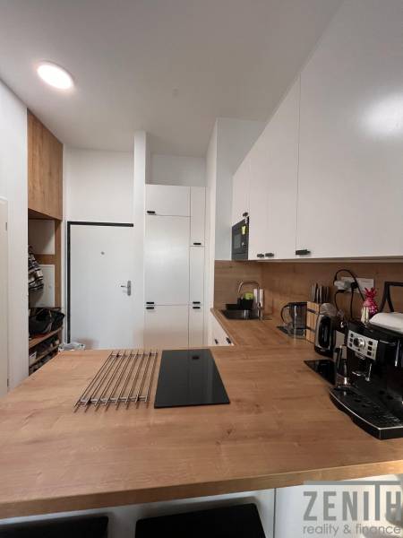 The interior of a kitchen in a one-room apartment with wooden decor and white cabinets.