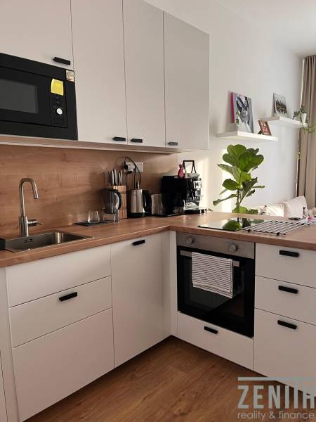 A kitchen in a studio apartment with white cabinets and a wood-patterned floor.