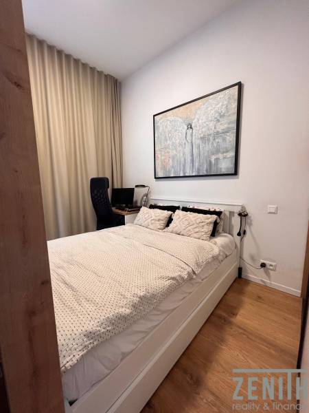 A bedroom with a bed, a desk, and a wooden decor floor in a studio apartment.