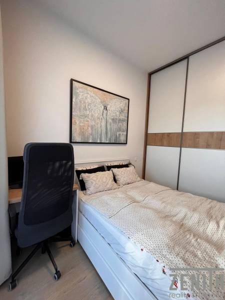 A bed with a desk, chair, and painting in a studio apartment with a wardrobe.