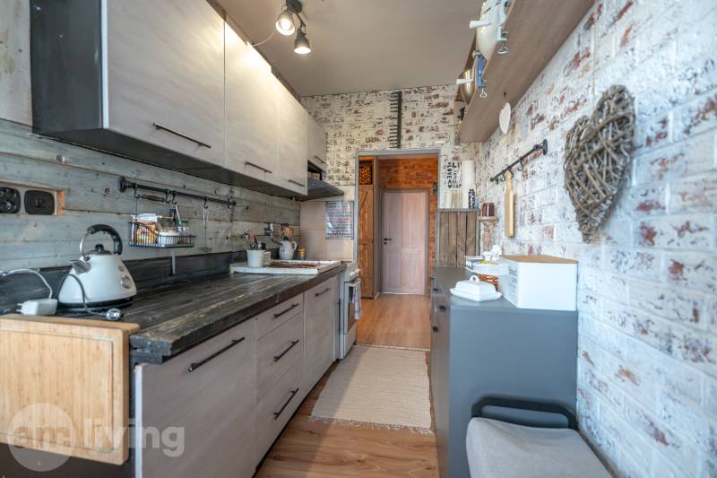 A kitchen in a three-room apartment with a wooden decor floor and a brick wall.