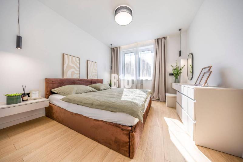 A bright bedroom with a comfortable bed, decorations, and a wooden-patterned floor in a 3-room apartment.