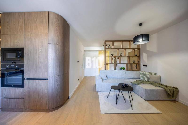 Living room in a 3-room apartment with a sofa, wooden decor, and a built-in kitchen.