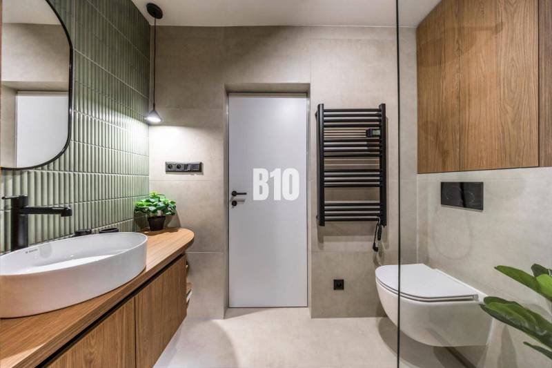 A bathroom in a 3-room apartment with wooden furniture, green tiles, and a wall-mounted drying rack.