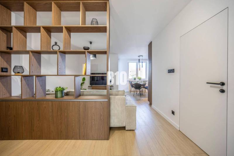 Interior of a 3-room apartment with an open living room, shelving wall, and flooring with a wooden decor.