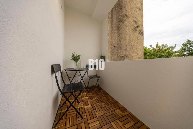 A balcony with two chairs and a table, flooring with a wooden decor in a three-room apartment.