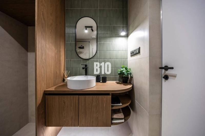 A bathroom with green tiles, an oval mirror, and a wooden-patterned floor.