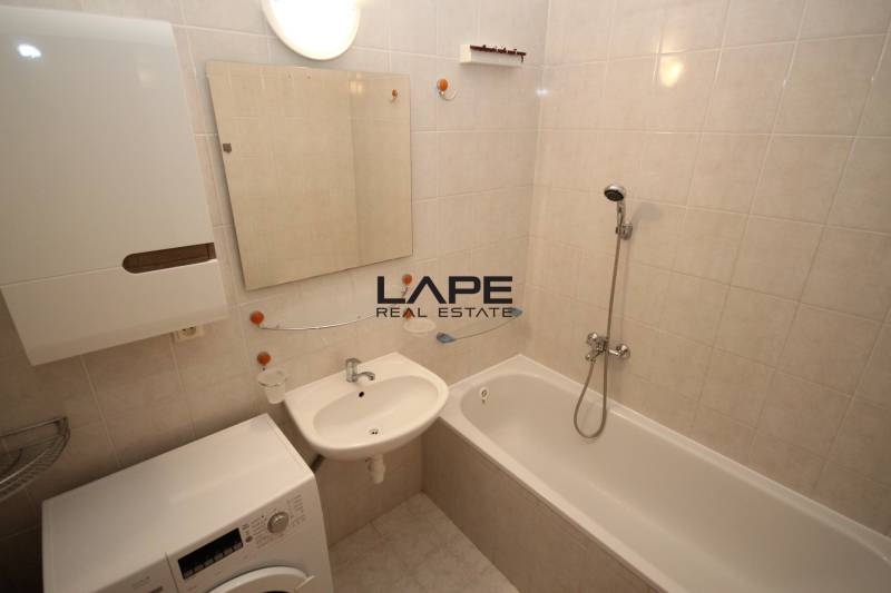 Bathroom in a studio apartment with a bathtub, washing machine, and sink on light tiles.