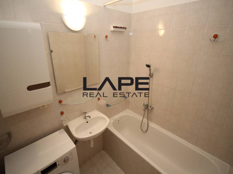 Bathroom in a studio apartment with a bathtub, sink, and washing machine, bright tiles.