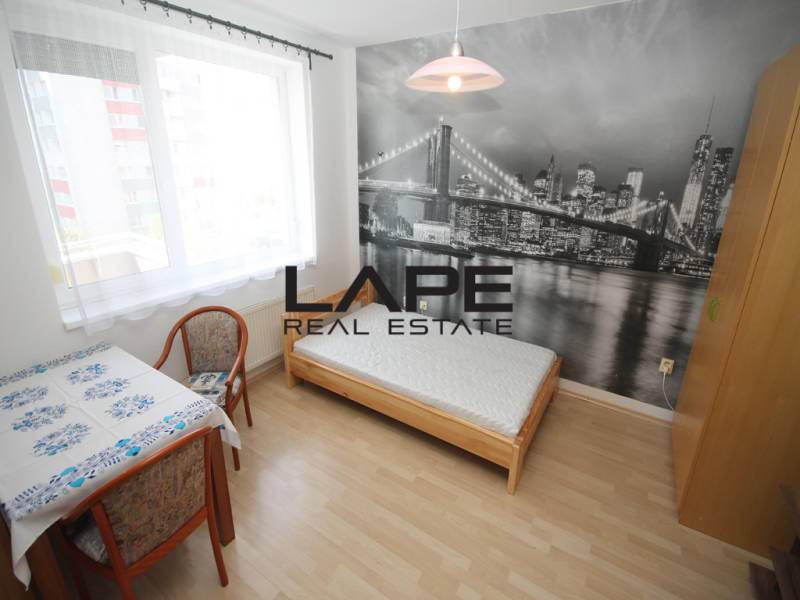 A room with a bed, a table, and a photo wallpaper of a bridge in a studio apartment, with a floor featuring a wooden decor.