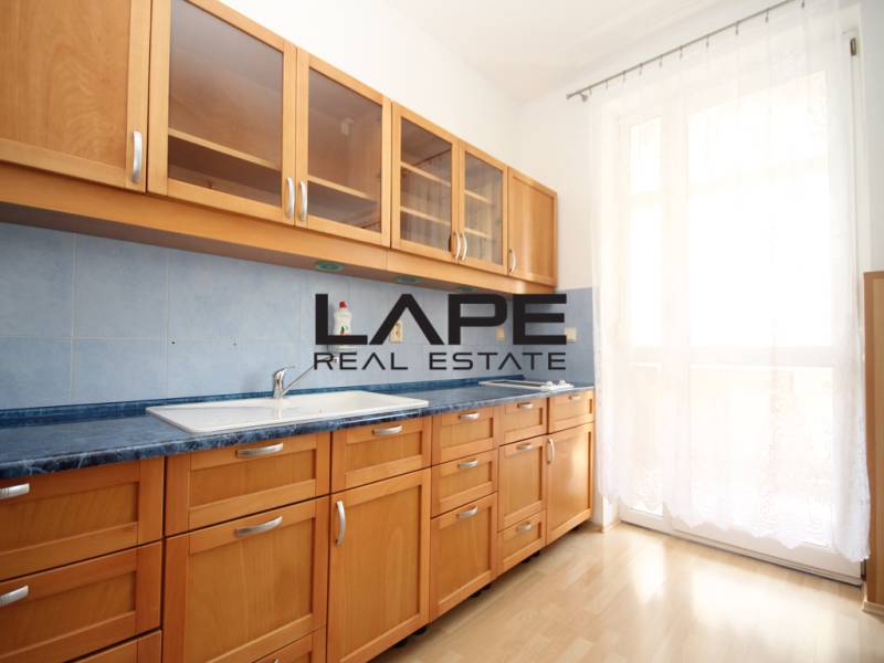 A kitchen in a studio apartment with wooden cabinets and a floor with a wood decor.