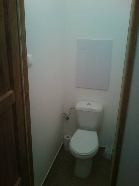 A toilet in a one-room apartment with a white wall and brown doors.