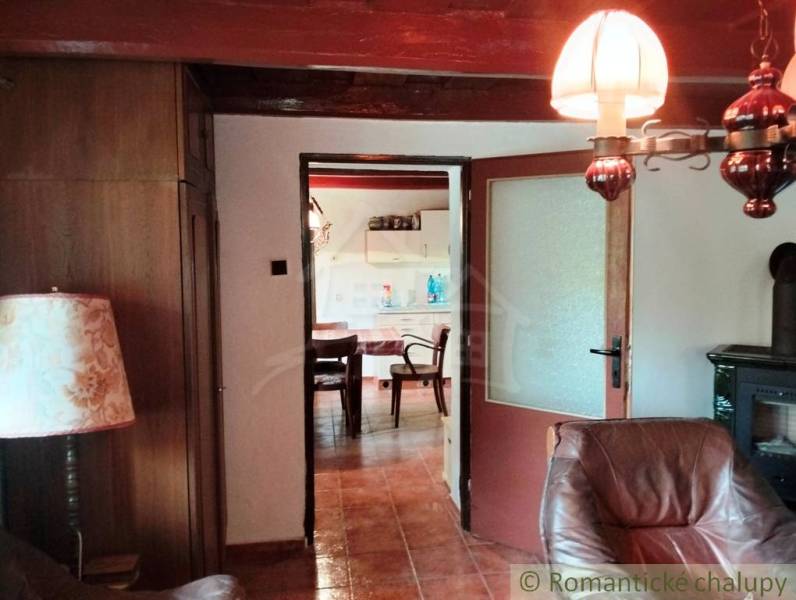 Interior of a cabin with a comfortable armchair, lamp, and a view into the kitchen.