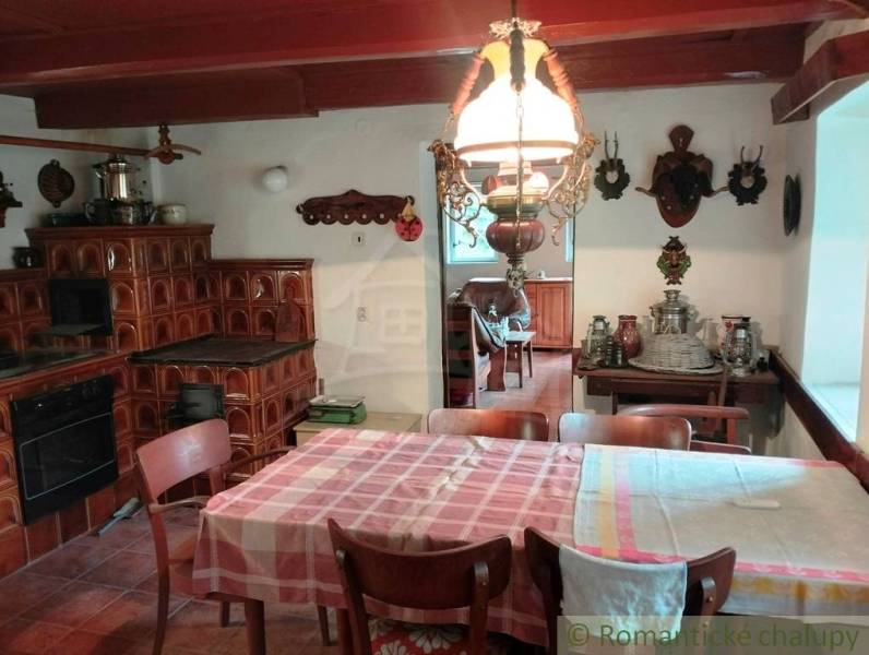 Rustic kitchen with a tiled stove and dining table in a cottage.