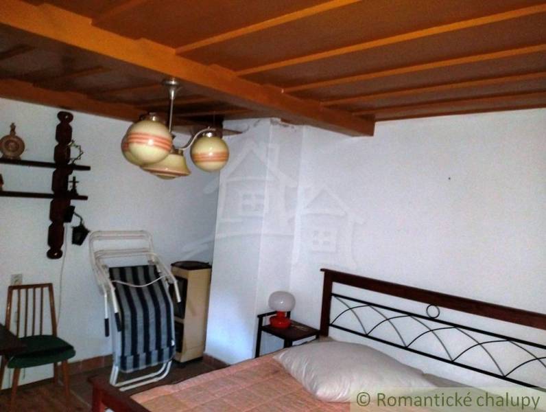 The interior of a cabin with a wooden ceiling, a bed, a small table, and ceramic lamps.