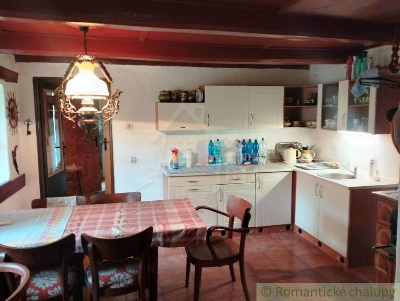 A kitchen in a cottage with a dining table, chairs, and rustic lighting.