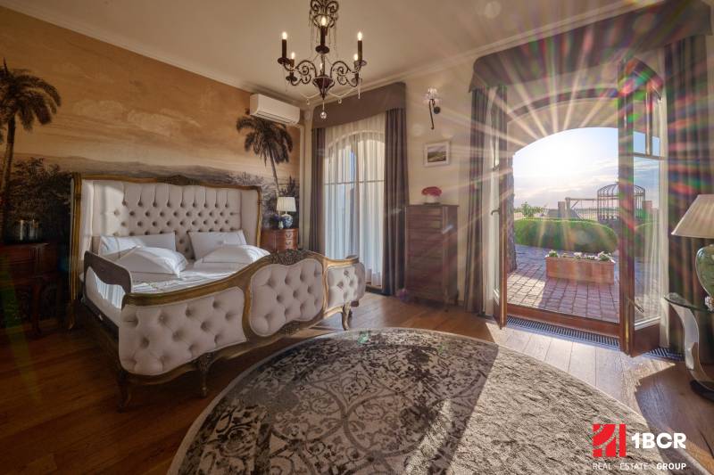 A bedroom in a villa with a bed, a wall mural of palm trees, and a wooden decor floor.