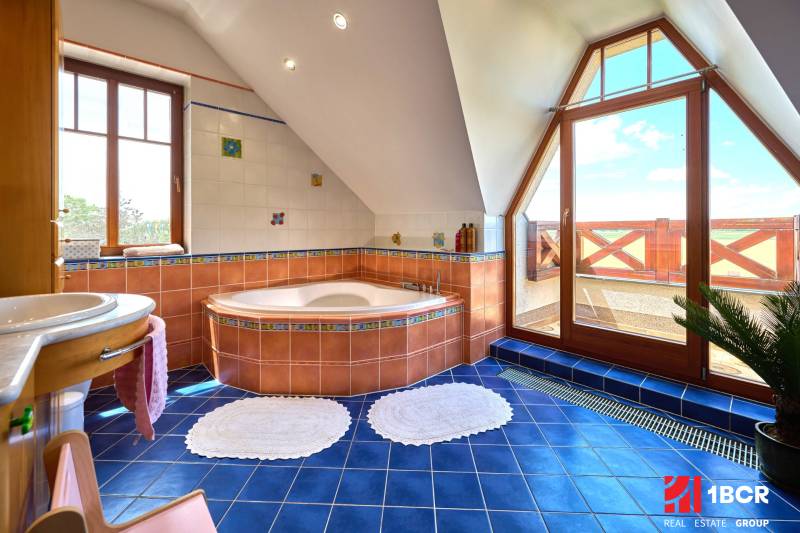Bathroom with a corner bathtub, blue tiles, and large windows in a villa.