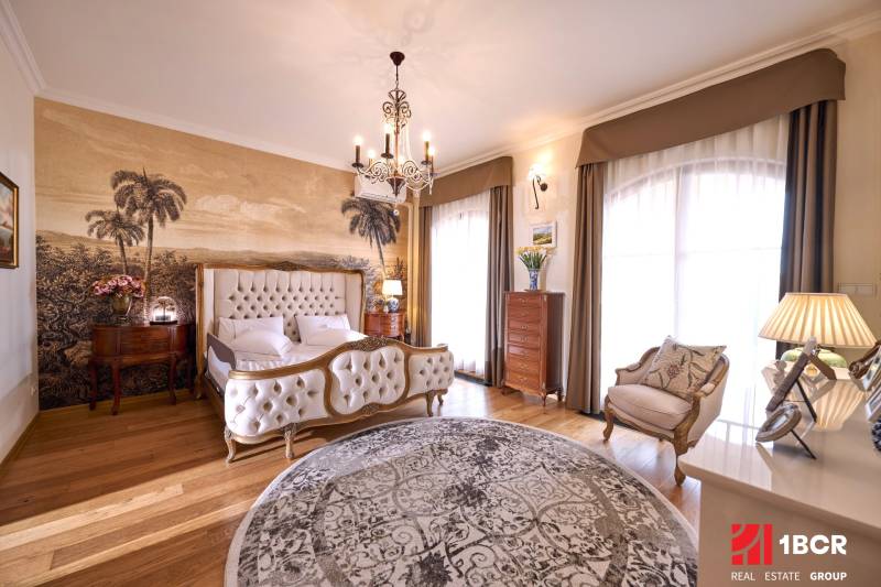 Luxury bedroom with an upholstered bed, palm wallpaper, and wood-patterned flooring.