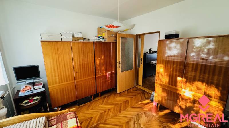 A room with furniture, wood-patterned flooring, and a television in a three-room apartment.