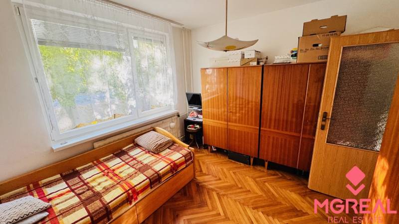 A room in a 3-room apartment with a wood-patterned floor, a bed, and a wardrobe.