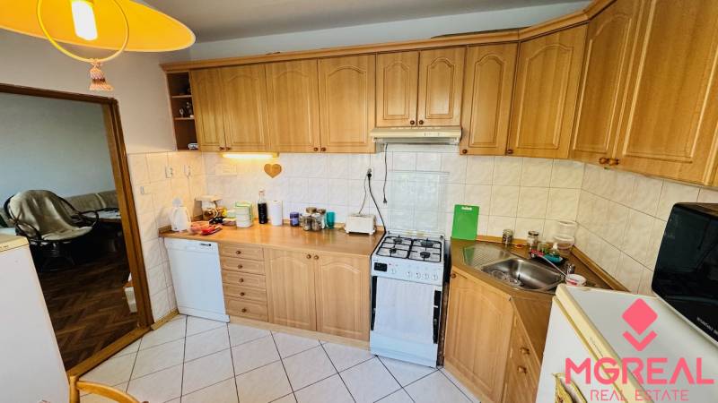 A kitchen with wooden decor, appliances, and a corner sink in a 3-room apartment.