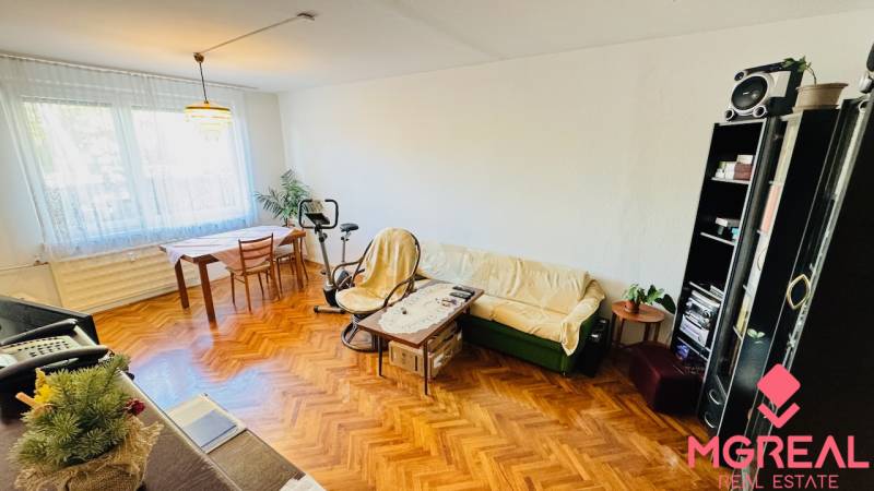 Living room with wood-patterned flooring in a 3-room apartment, includes a couch and a table.