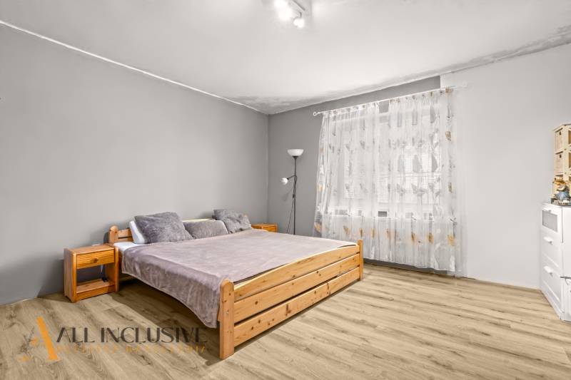 A bedroom in a family house with a bed, a wooden decor floor, and light curtains.