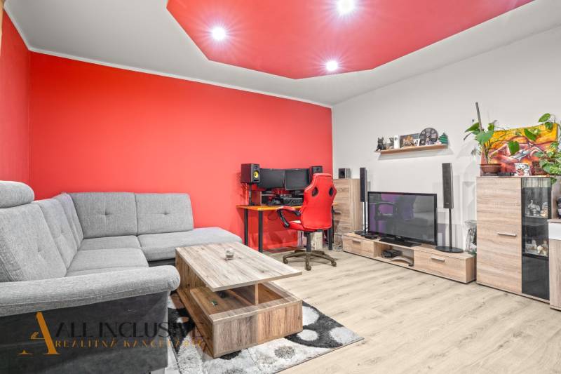 Living room in a family house with a red wall, gray sofa, and wooden decor flooring.