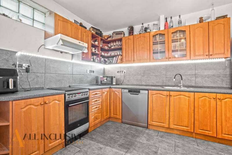A kitchen in a family house with wooden decor, appliances, and gray tiles.