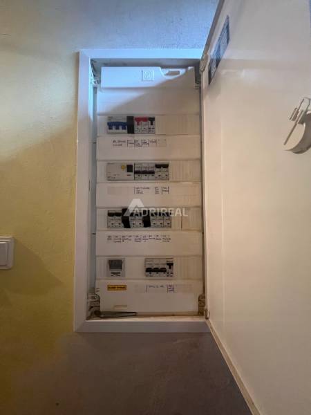 An open electrical panel in a family house with attached labels and white walls.