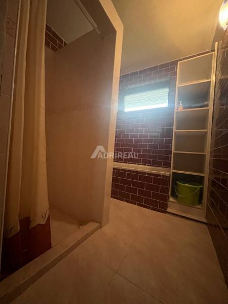 Bathroom with tiles, shower enclosure, and a shelf in a family house.