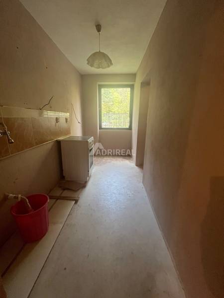 A narrow room in a family house with a single-pane window and a ceiling light, in need of renovation.