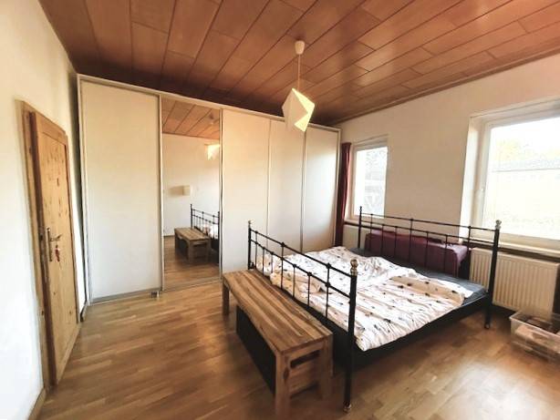 Bedroom with a metal bed and a wardrobe, floor with wooden decor in a family house.