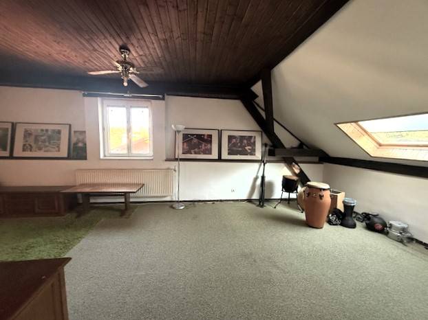 Attic room with carpeted floor, ceiling fan, and drums in a family house.