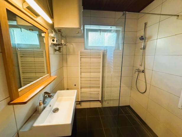 A bathroom in a family house with a shower, a sink, and a window, with a wooden decor floor.