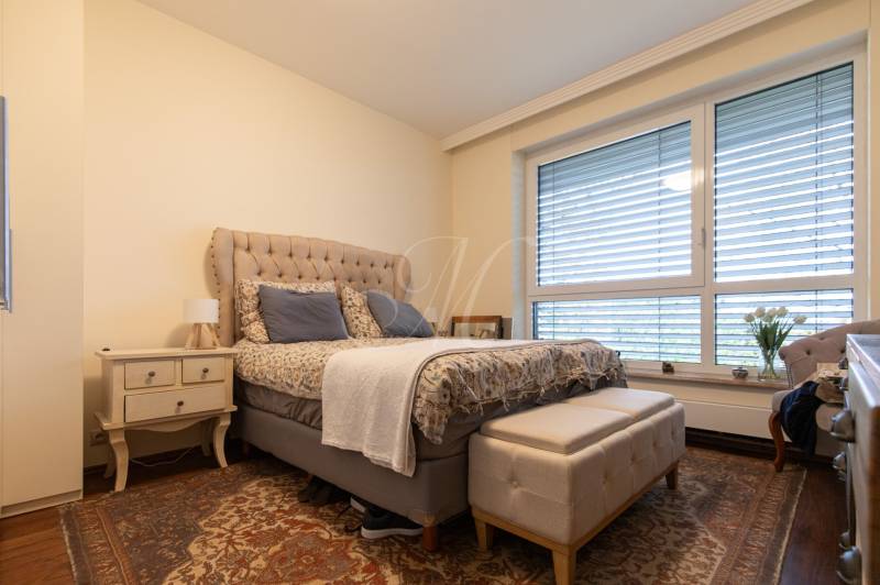 A bedroom with a comfortable bed, a nightstand, and a floor with a wooden decor in a 3-room apartment.