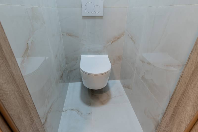 A toilet with ceramic tiles in a 3-room apartment, white sanitary equipment.