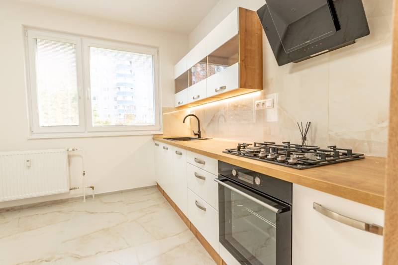 A kitchen in a 3-room apartment with a gas stove, wooden decor, and white cabinets.