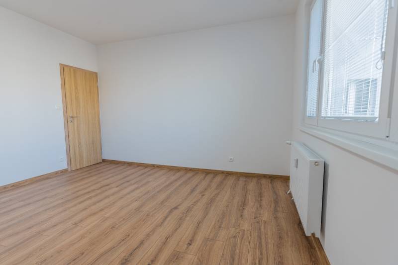 A room in a 3-room apartment with a wooden decor floor, white walls, and a radiator.