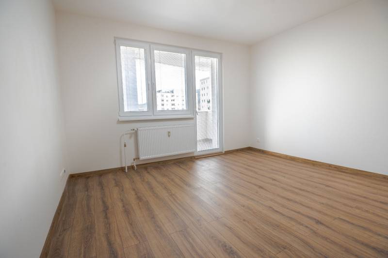 An empty room with a wooden floor and a French window in a 3-room apartment.