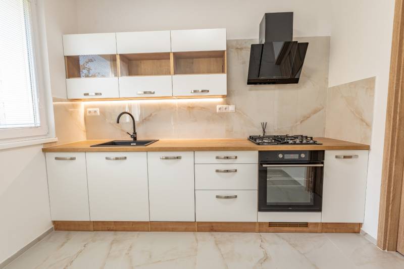 A kitchen with white cabinets, a black range hood, a cooktop, and a floor with a wood design.