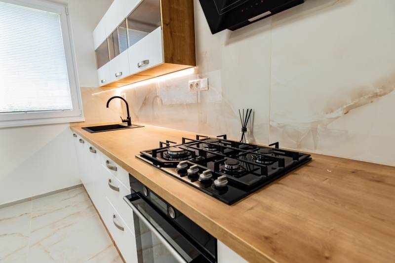 A kitchen in a 3-room apartment with a wood-patterned floor, a built-in cooktop, and a wooden countertop.